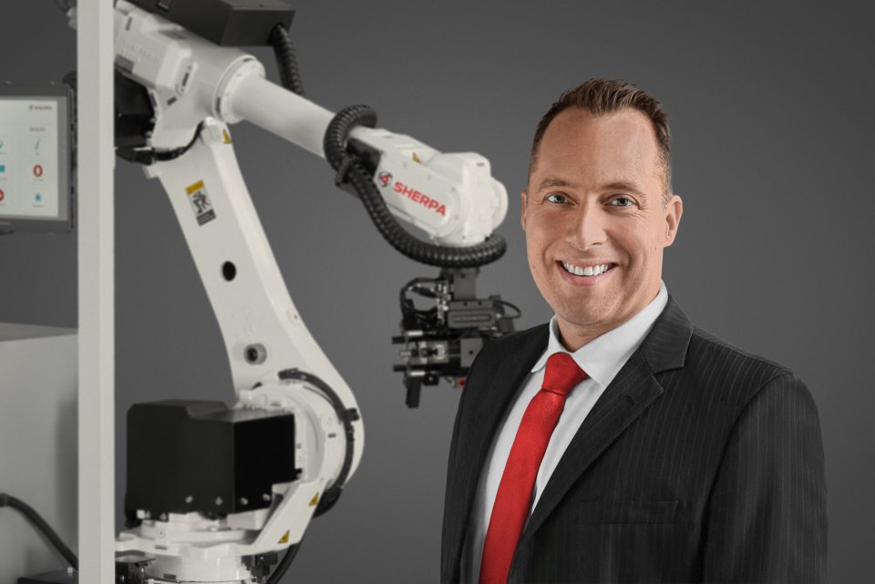 Dr. Eike Langenberg, der sich rechts im Bild neben einem Roboter-Greifarm befindet.